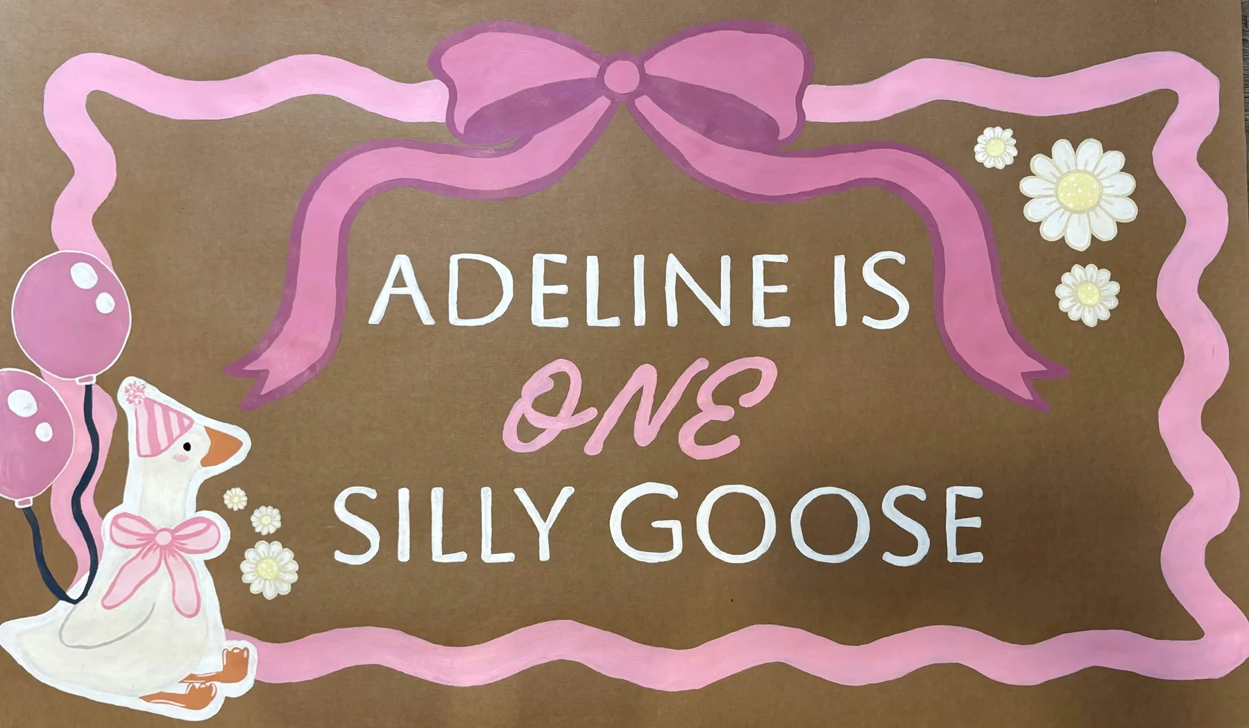 Hand-painted pink first birthday banner reading Adeline Is One Silly Goose, decorated with a bow, balloons, daisies, and a party goose